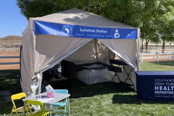 “Lactation Station” provided by the Southwest Utah Public Health Department. The image shows a pop-up tent setup outdoors labeled “Lactation Station,” with a table displaying informational materials.