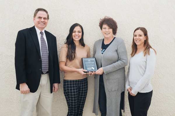 Four people standing indoors, smiling at the camera, holding a plaque for a USU Extension partnership recognition.
