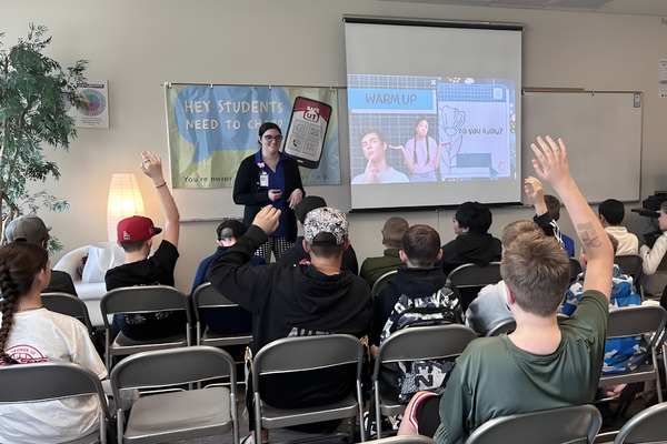 A presenter speaking to a classroom of students, some with hands raised, during a vape prevention session.