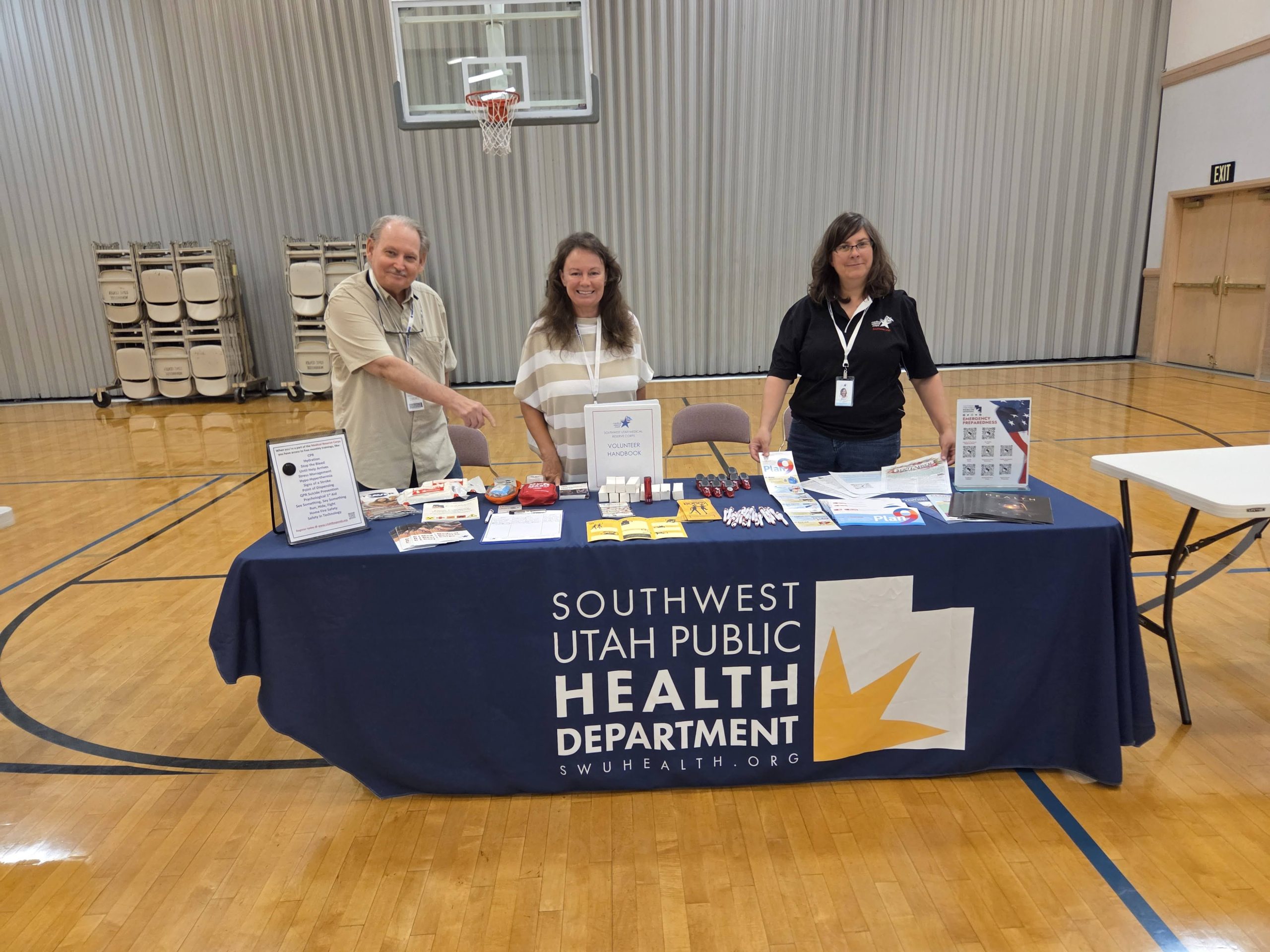 Volunteers standing behind a Southwest Utah Public Health Department table at a community event, providing information to attendees.