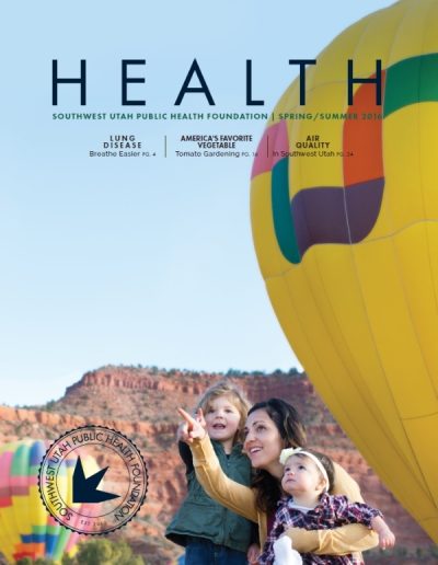 Front cover of "HEALTH" magazine by the Southwest Utah Public Health Foundation, Spring/Summer 2016 issue. The photograph shows a mother and her two young children watching hot air balloons, with a young girl pointing upward toward a large yellow hot air balloon in the foreground against a background of desert red rock cliffs.