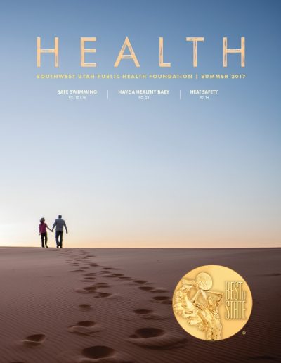 Front cover of "HEALTH" magazine by the Southwest Utah Public Health Foundation, Summer 2017 issue. The main photograph shows a couple holding hands as they walk away across a vast desert sand dune under a wide, clear blue-to-orange gradient sky. A line of footprints stretches behind them.
