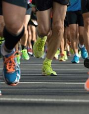 Close-up view focusing on the colorful running shoes of a crowd of marathon participants running on asphalt during a race.