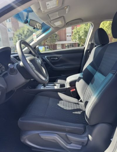 Interior front cabin view of a 2018 Nissan Altima showing black cloth driver and passenger seats, steering wheel, and dashboard.